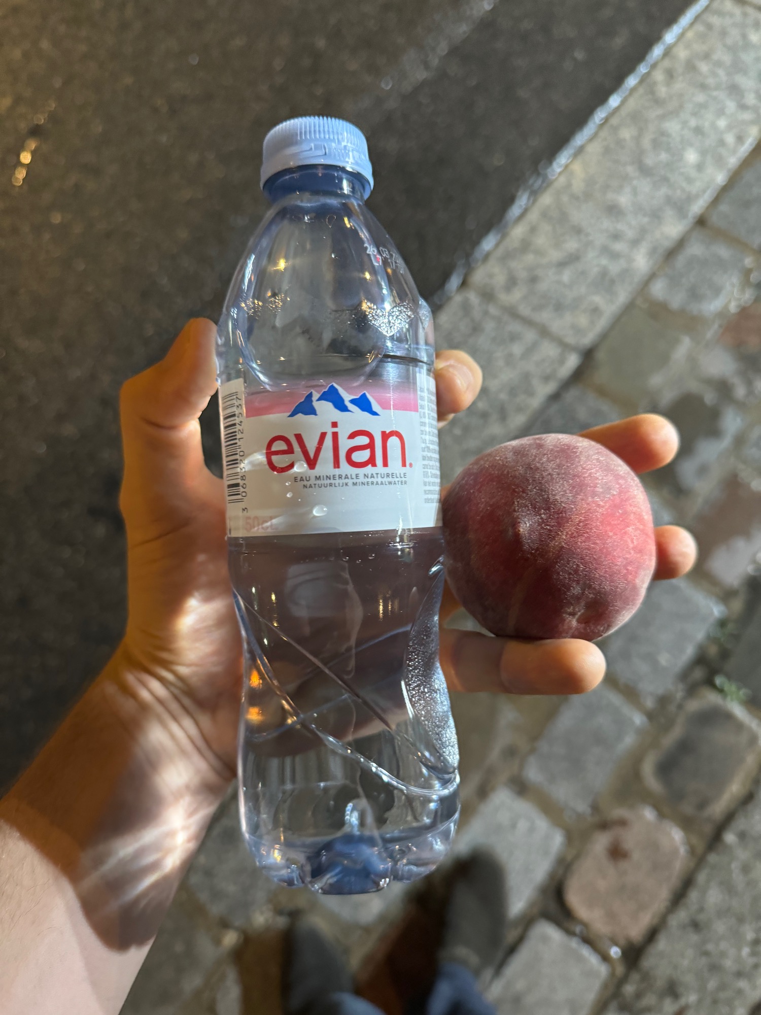 a hand holding a bottle of water and a peach