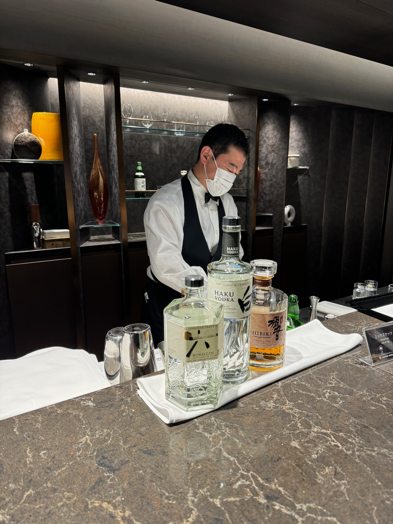 a man wearing a face mask standing behind a bar with bottles of alcohol