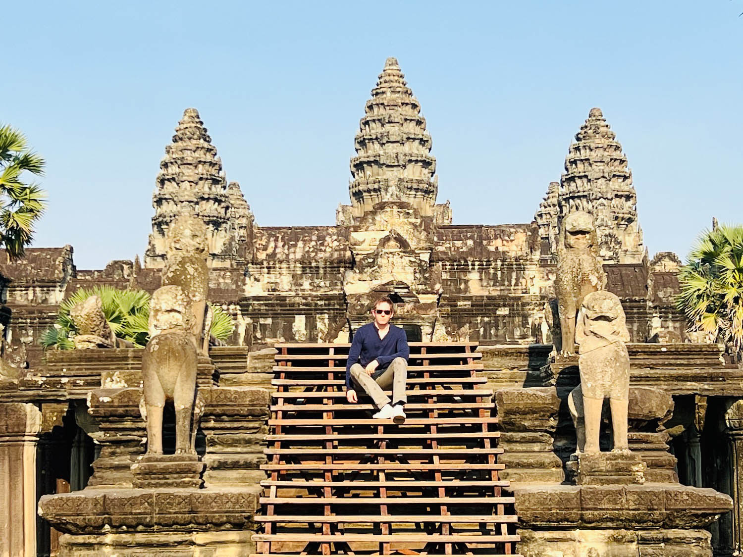 a man sitting on a wooden staircase in front of a stone building with Angkor Wat in the background