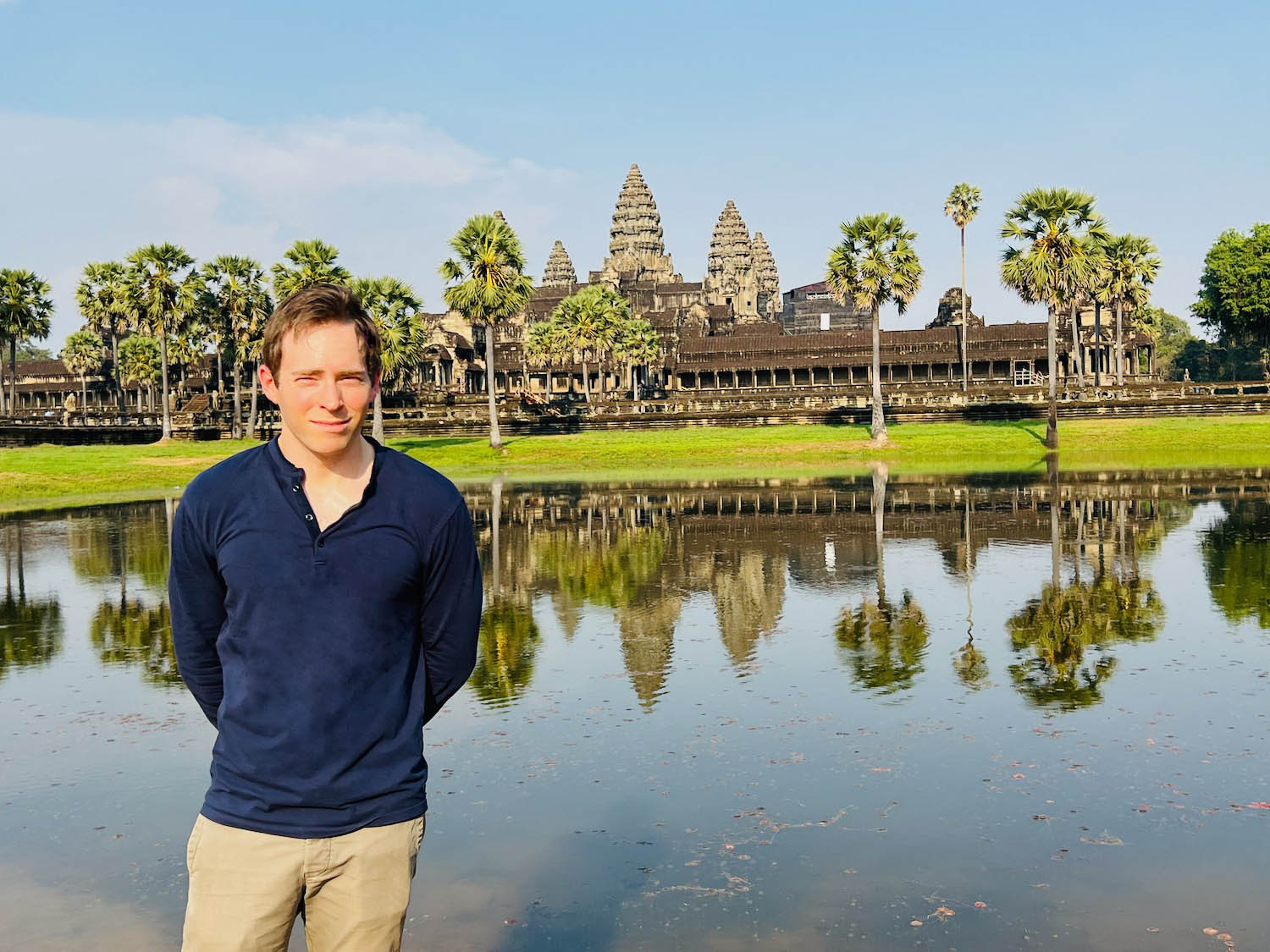 a man standing in front of a body of water with Angkor Wat in the background