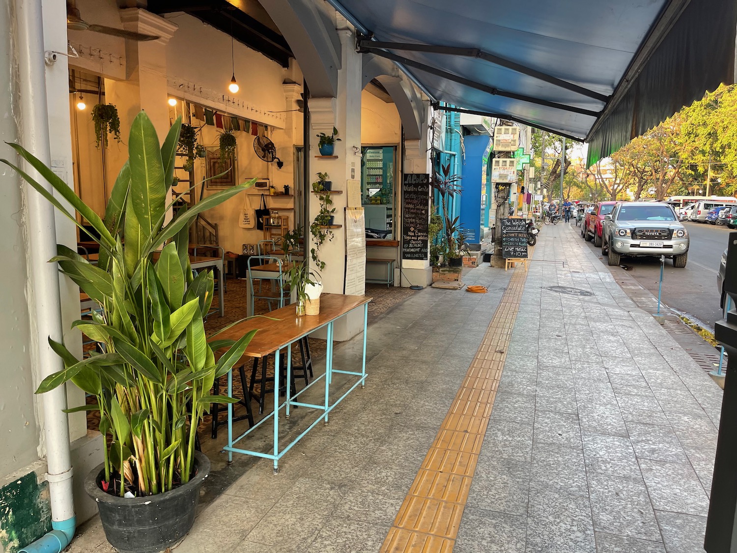 a street with cars and a sidewalk with tables and plants