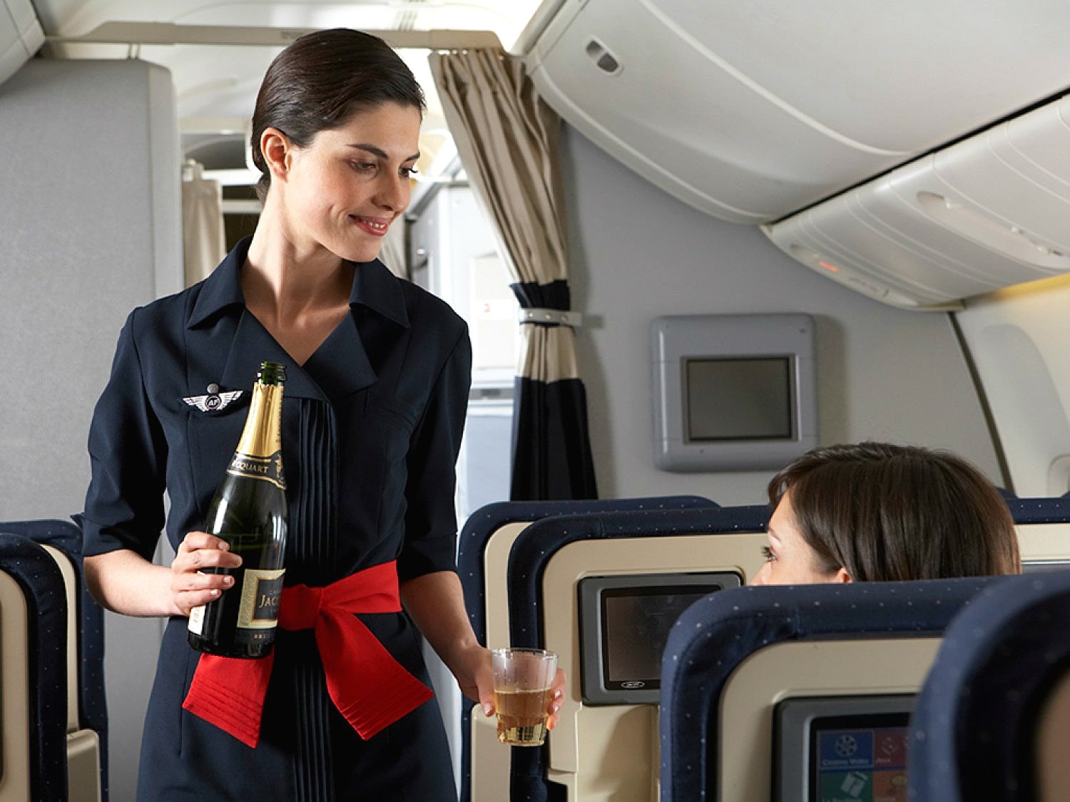 a woman holding a bottle and a glass in an airplane