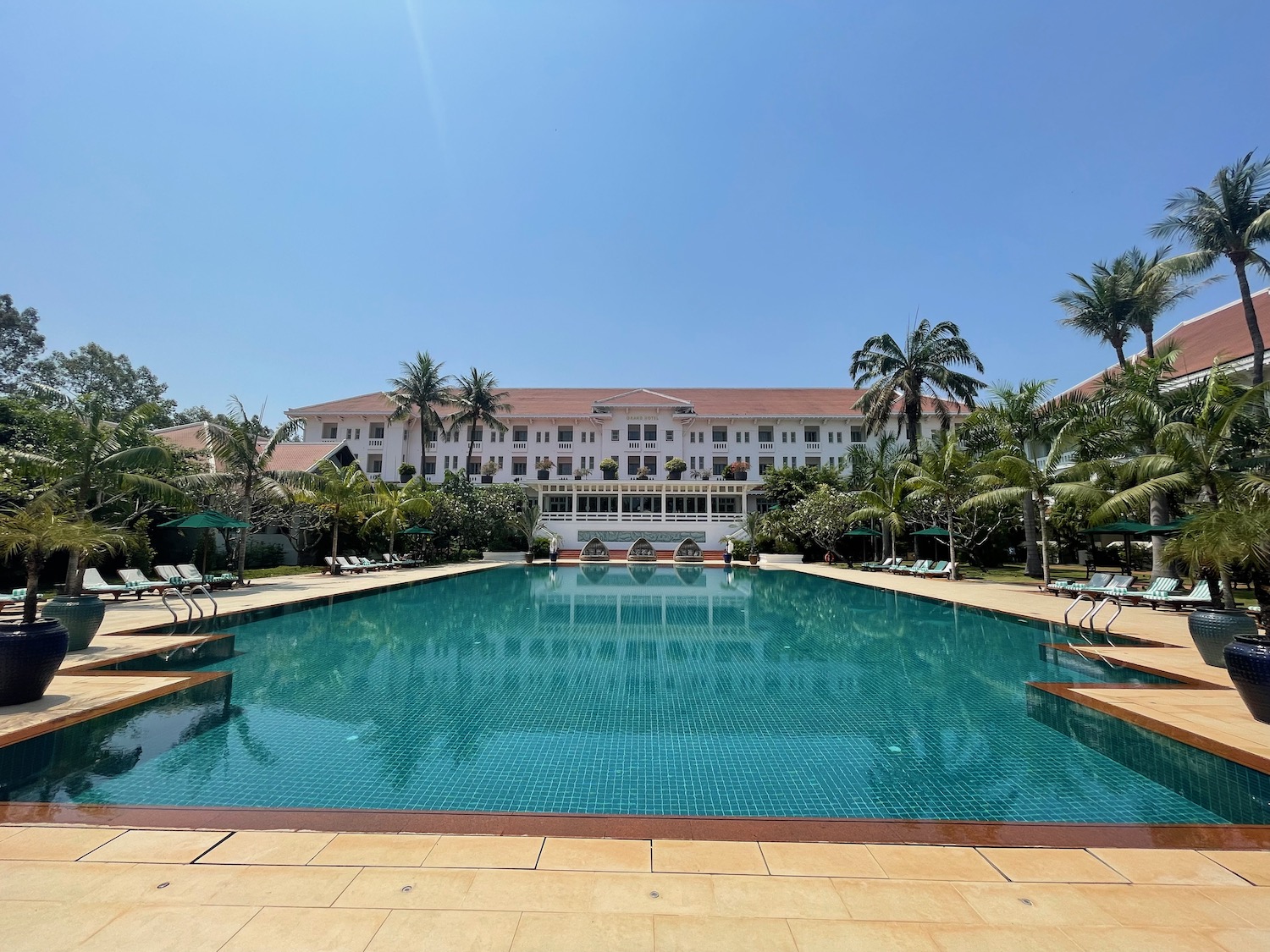 a pool with chairs and palm trees in front of a building