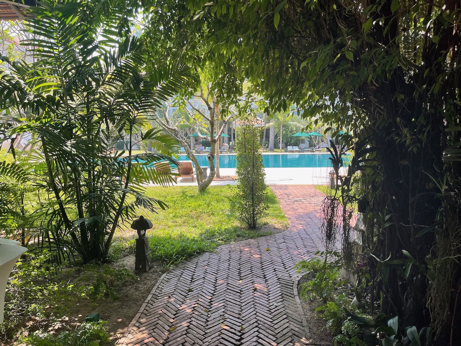 a brick path with trees and a pool in the background