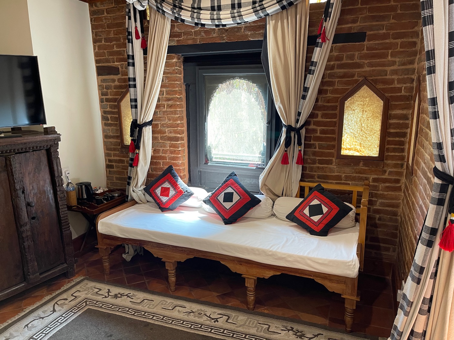 a bed with pillows in a room with a brick wall and a window