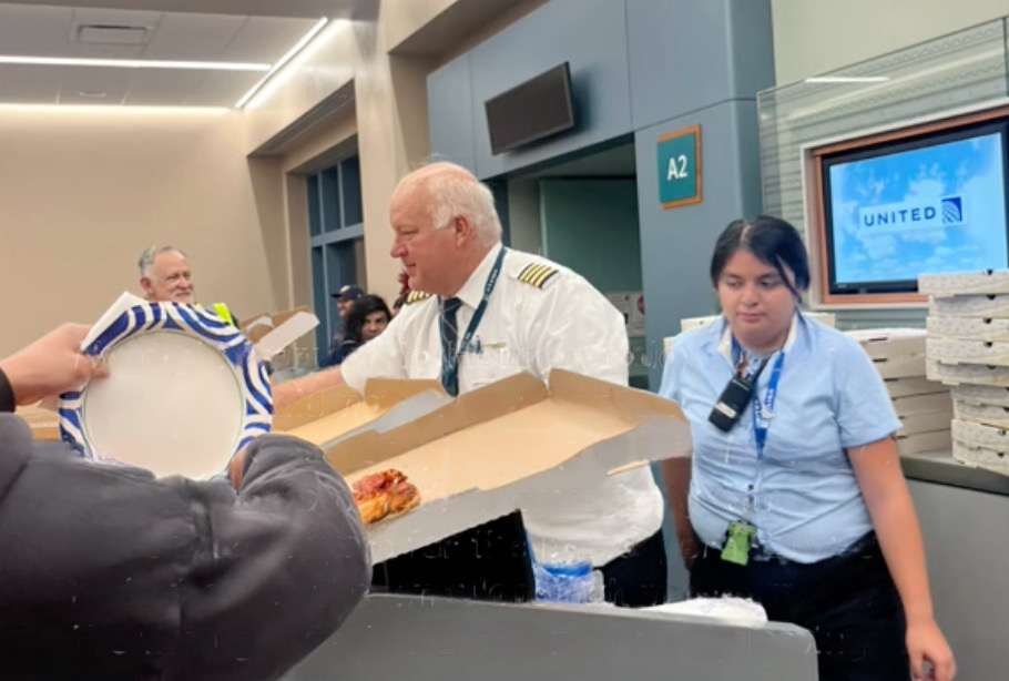 a group of people standing around a table with a pizza box