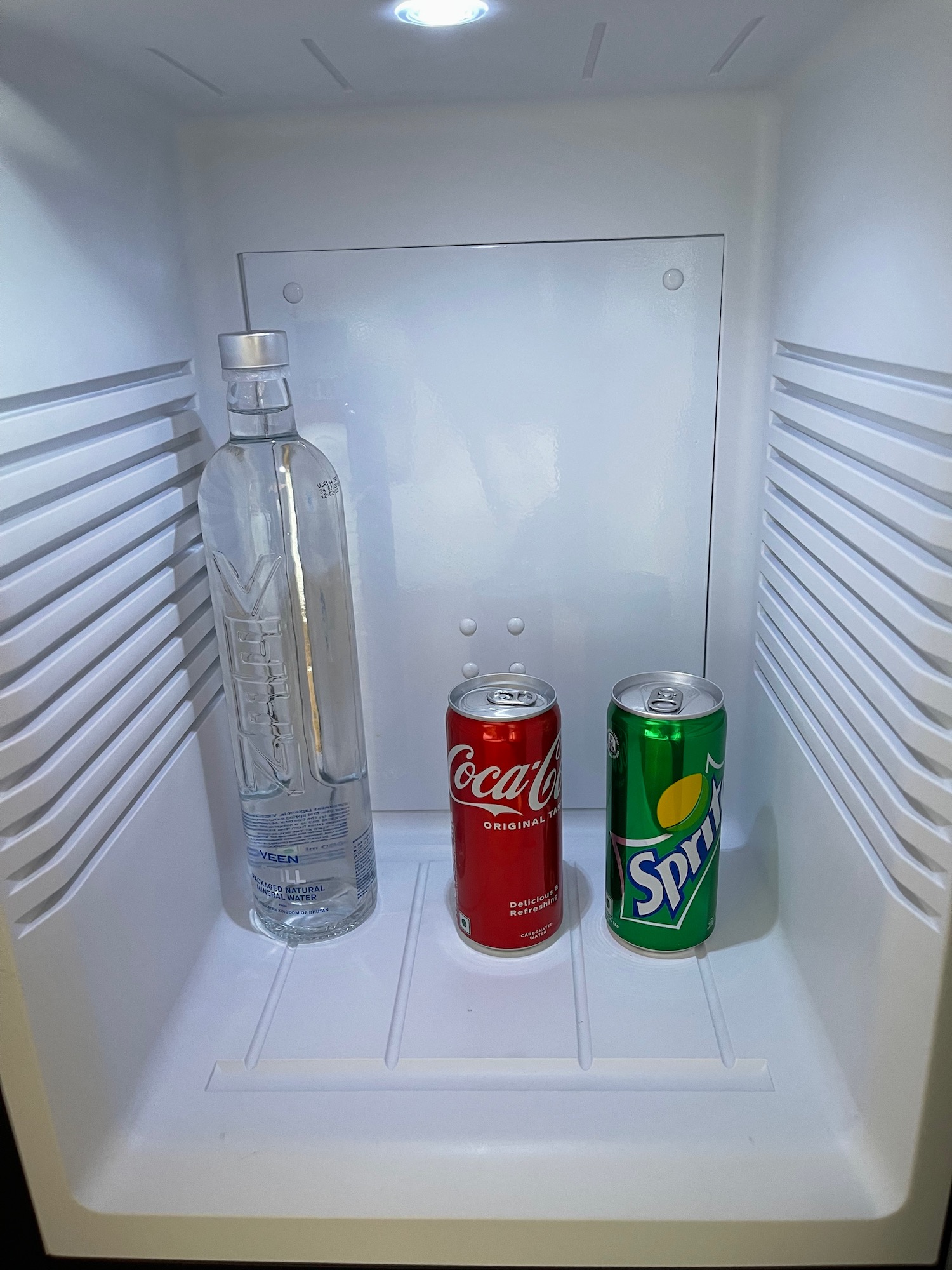 a bottle and cans of soda in a refrigerator