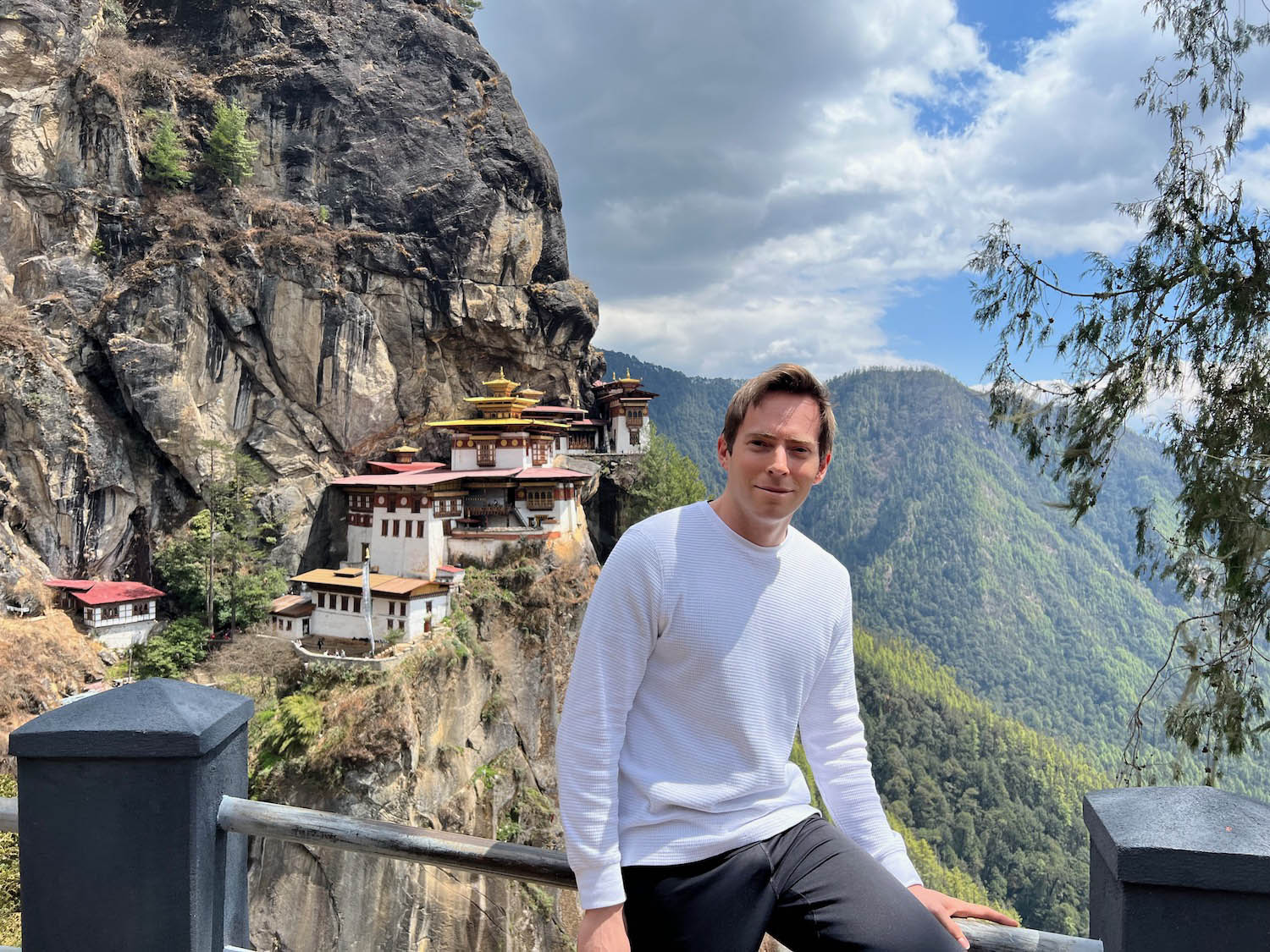 a man posing for a picture with a building on the side of a cliff