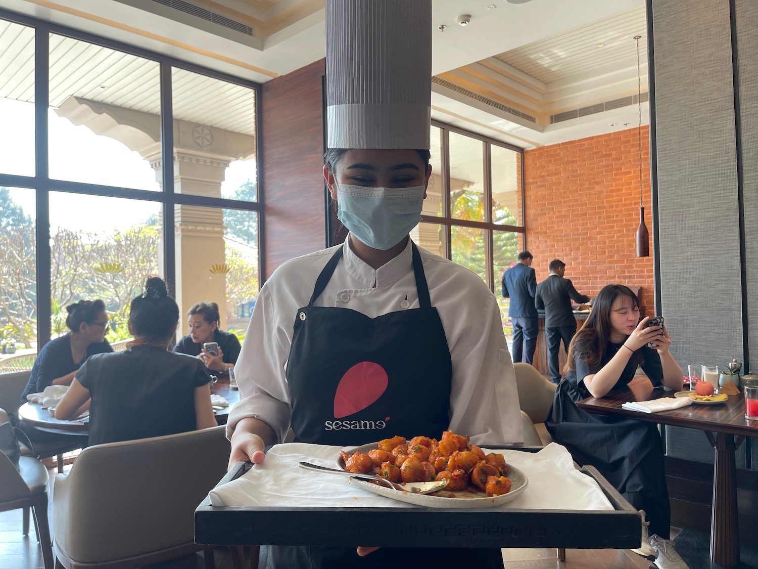 a person wearing a mask and a chef hat holding a tray of food