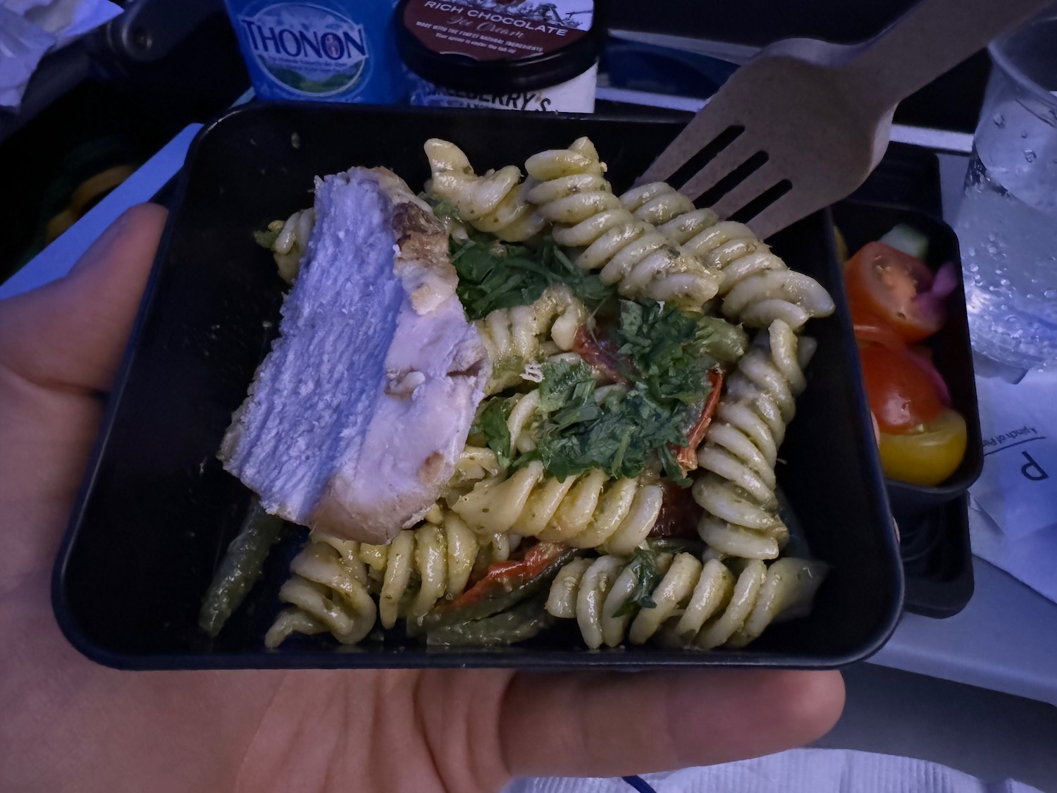 a hand holding a black bowl of pasta with meat and vegetables