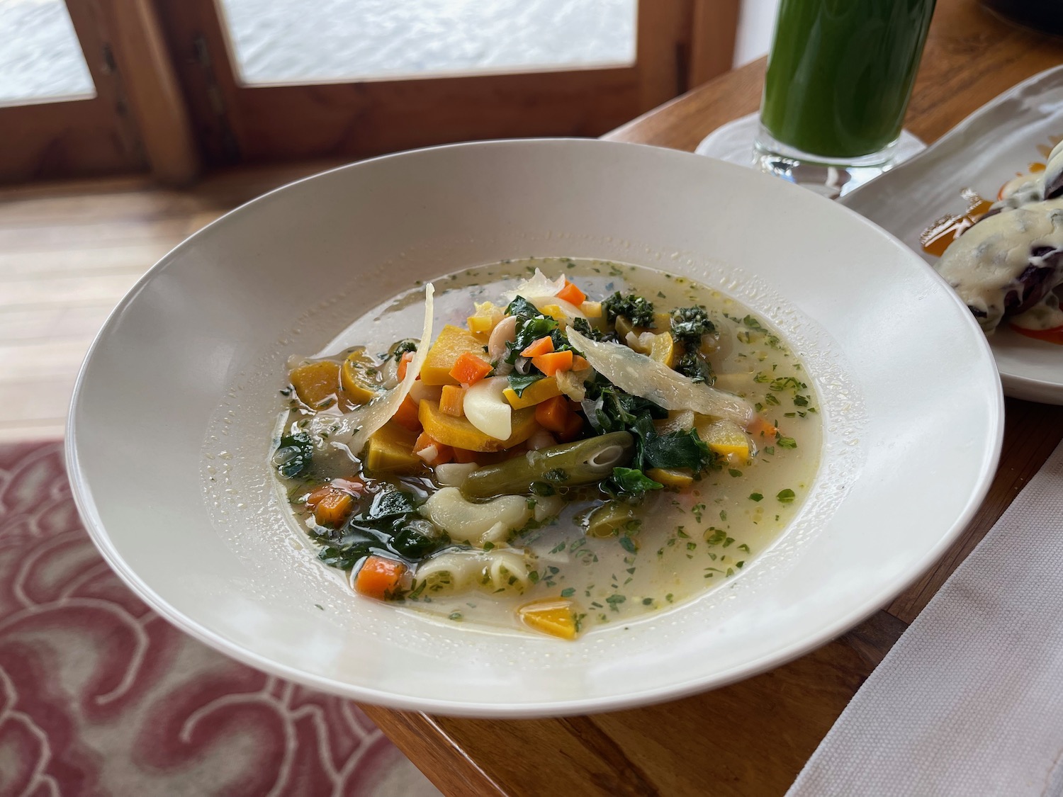 a bowl of soup with vegetables and a glass of green juice