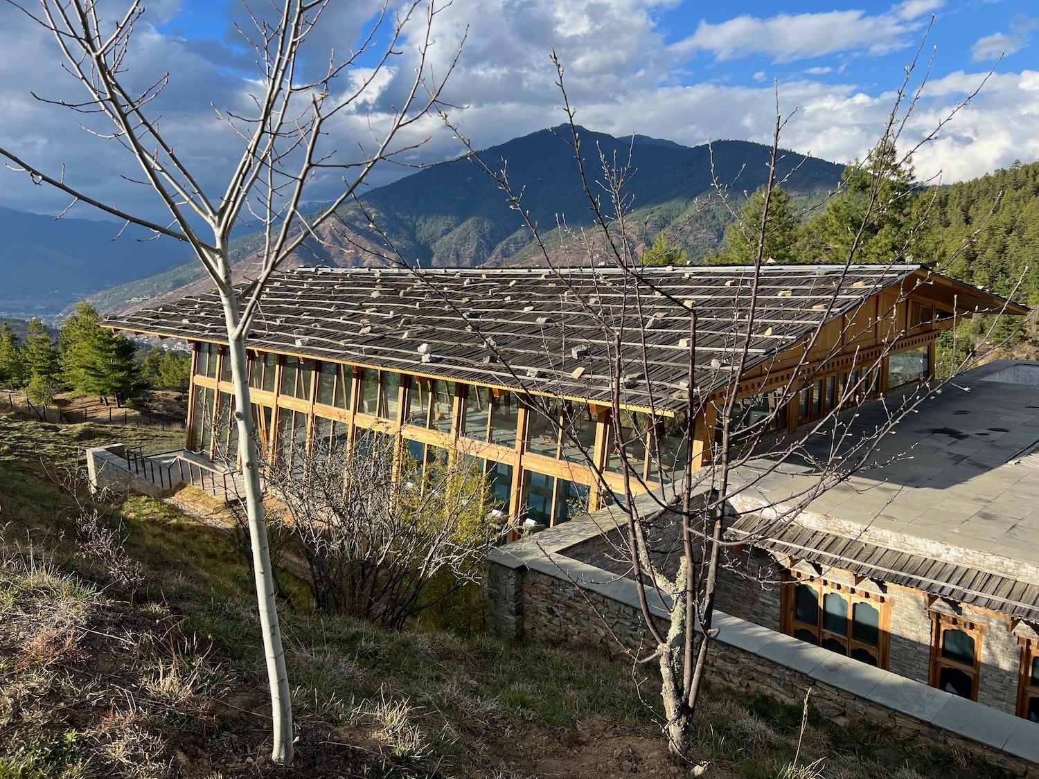 a building with a roof and trees and mountains in the background