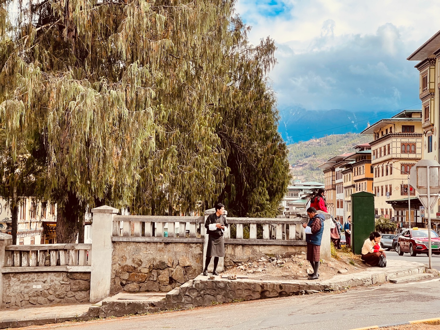 a group of people standing on a sidewalk by a stone wall