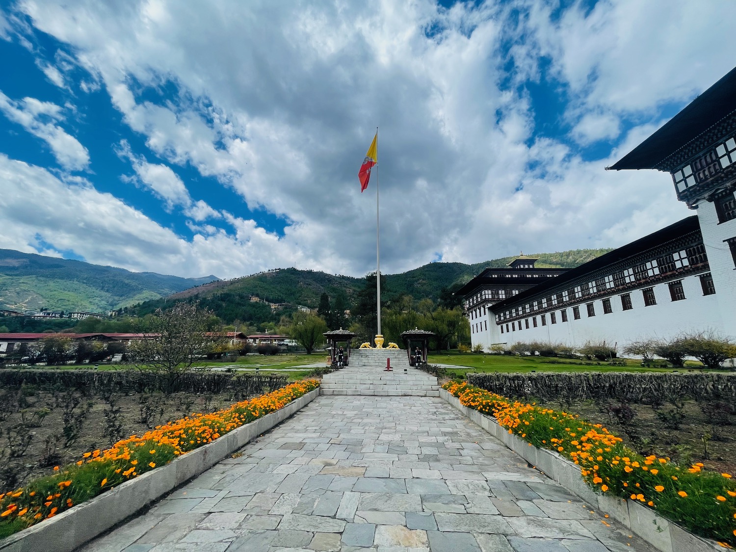 a stone walkway with a flag pole and flowers in front of a building