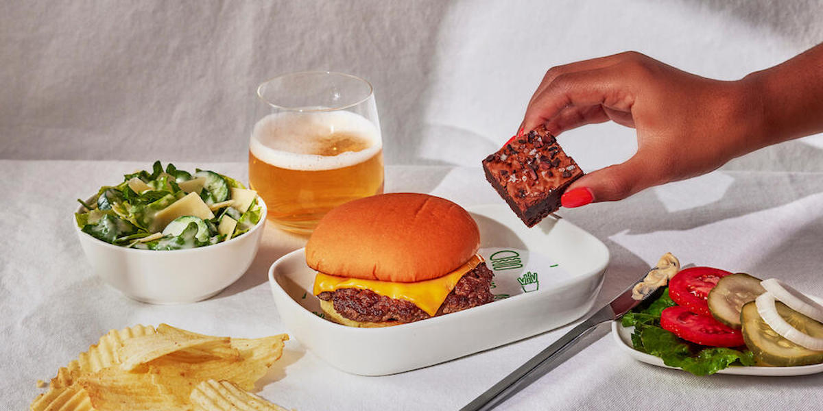 a hand holding a brownie over a burger