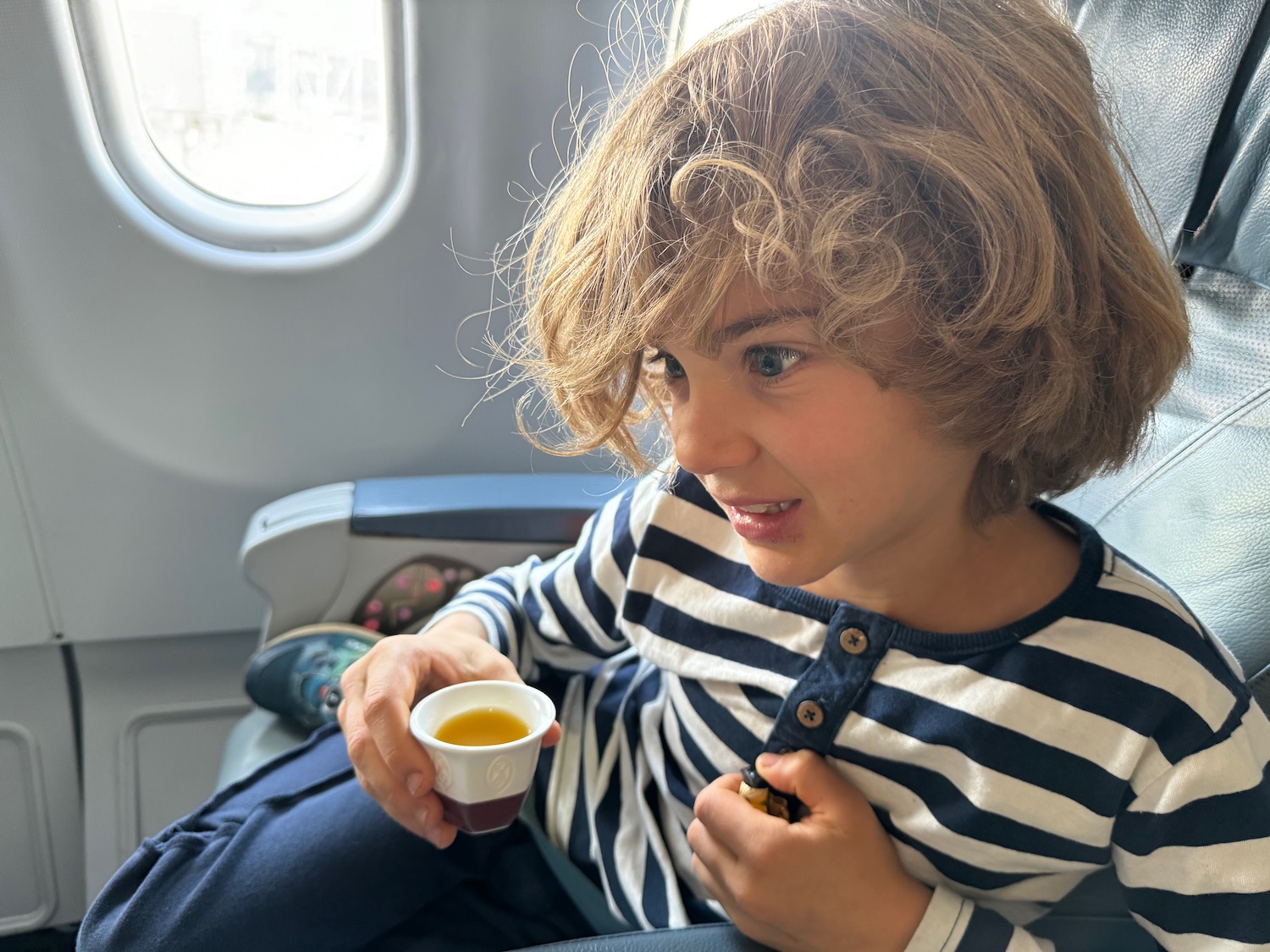 a child sitting in an airplane holding a small cup of liquid