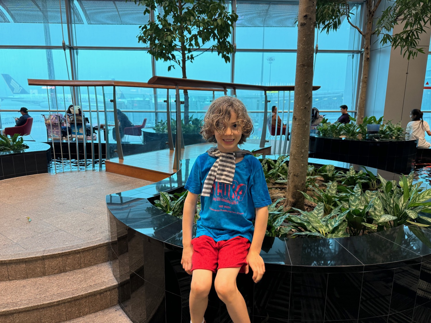 a boy sitting on a black circular object with plants in front of him