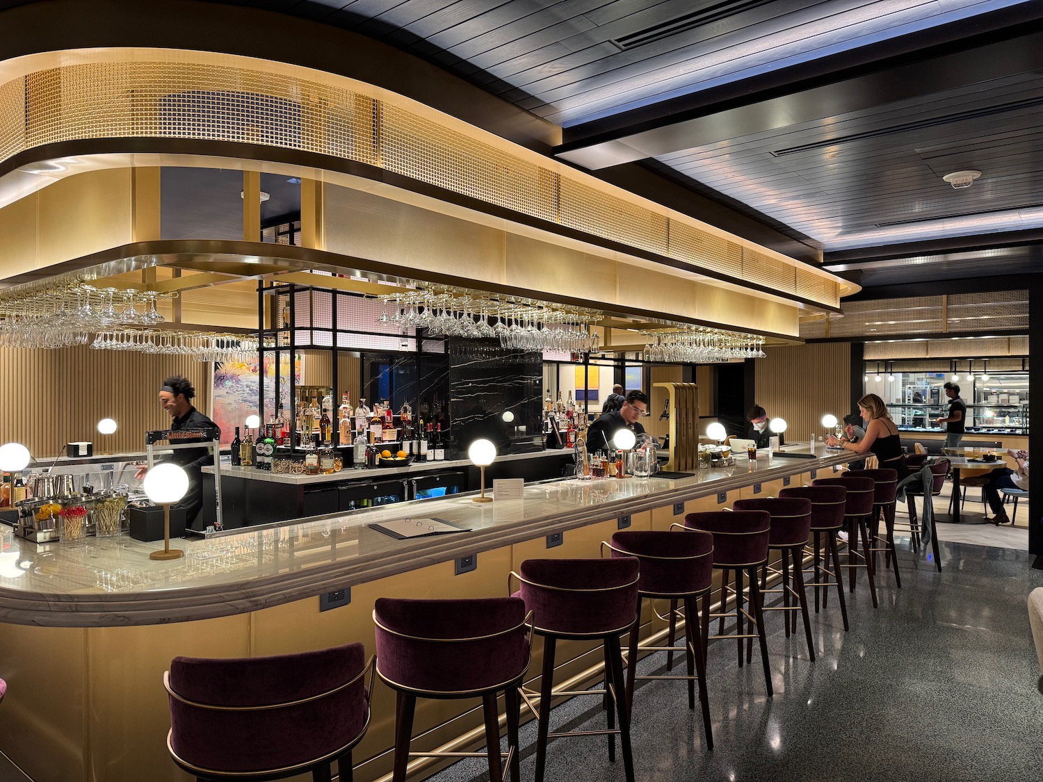 a bar with wine glasses and people sitting at the counter