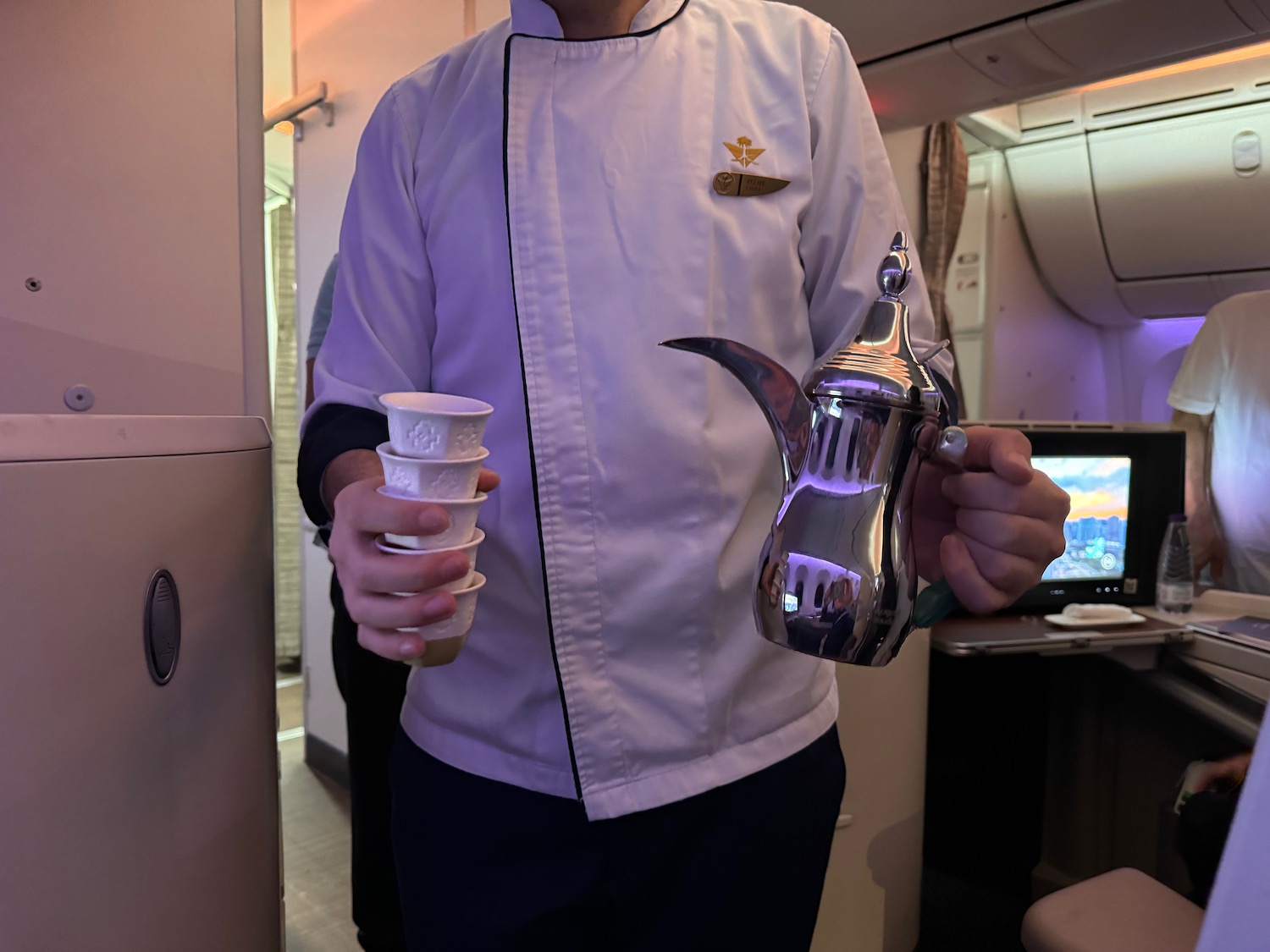 a man in a white coat holding a coffee pot and a cup