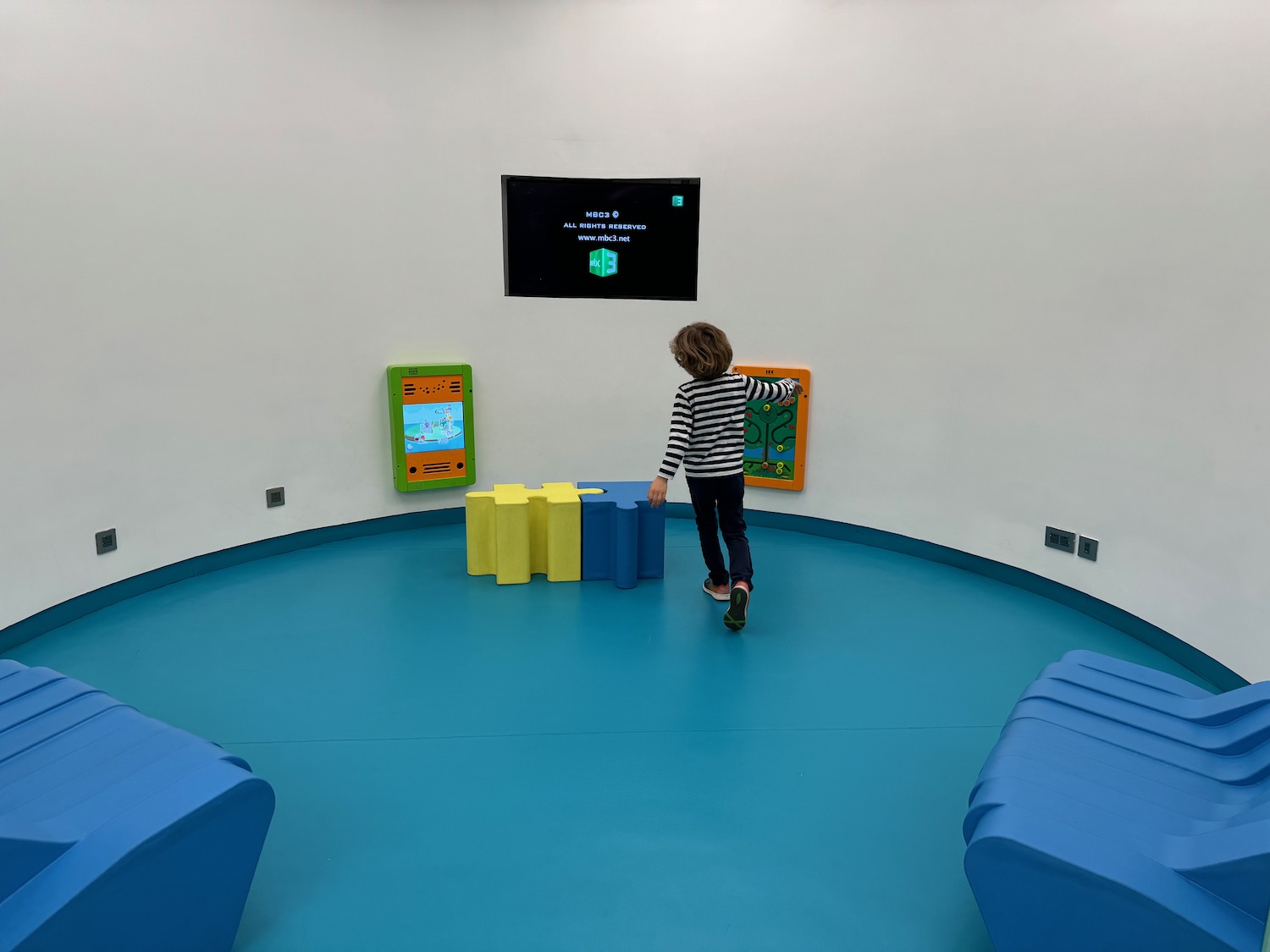 a child walking in a room with blue chairs and a television