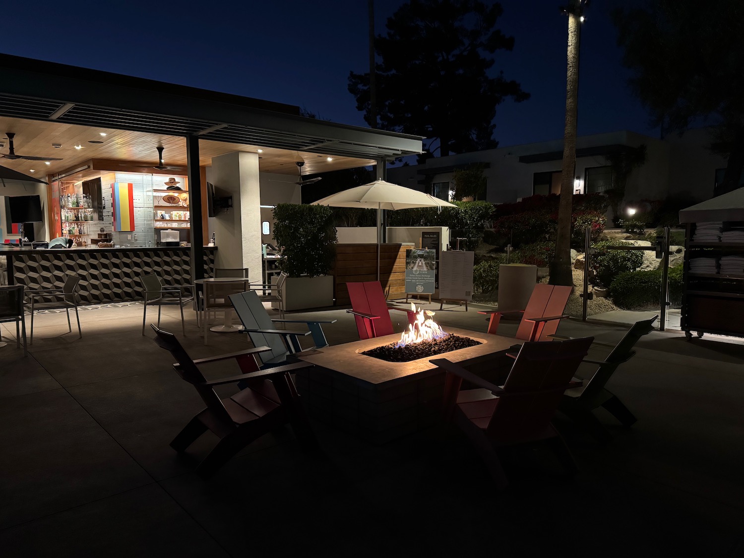 a fire pit with chairs and umbrellas in front of a building