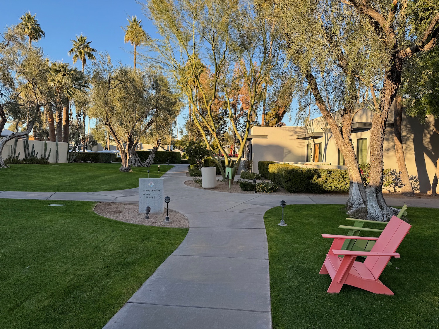 a walkway with a pink chair and green lawn