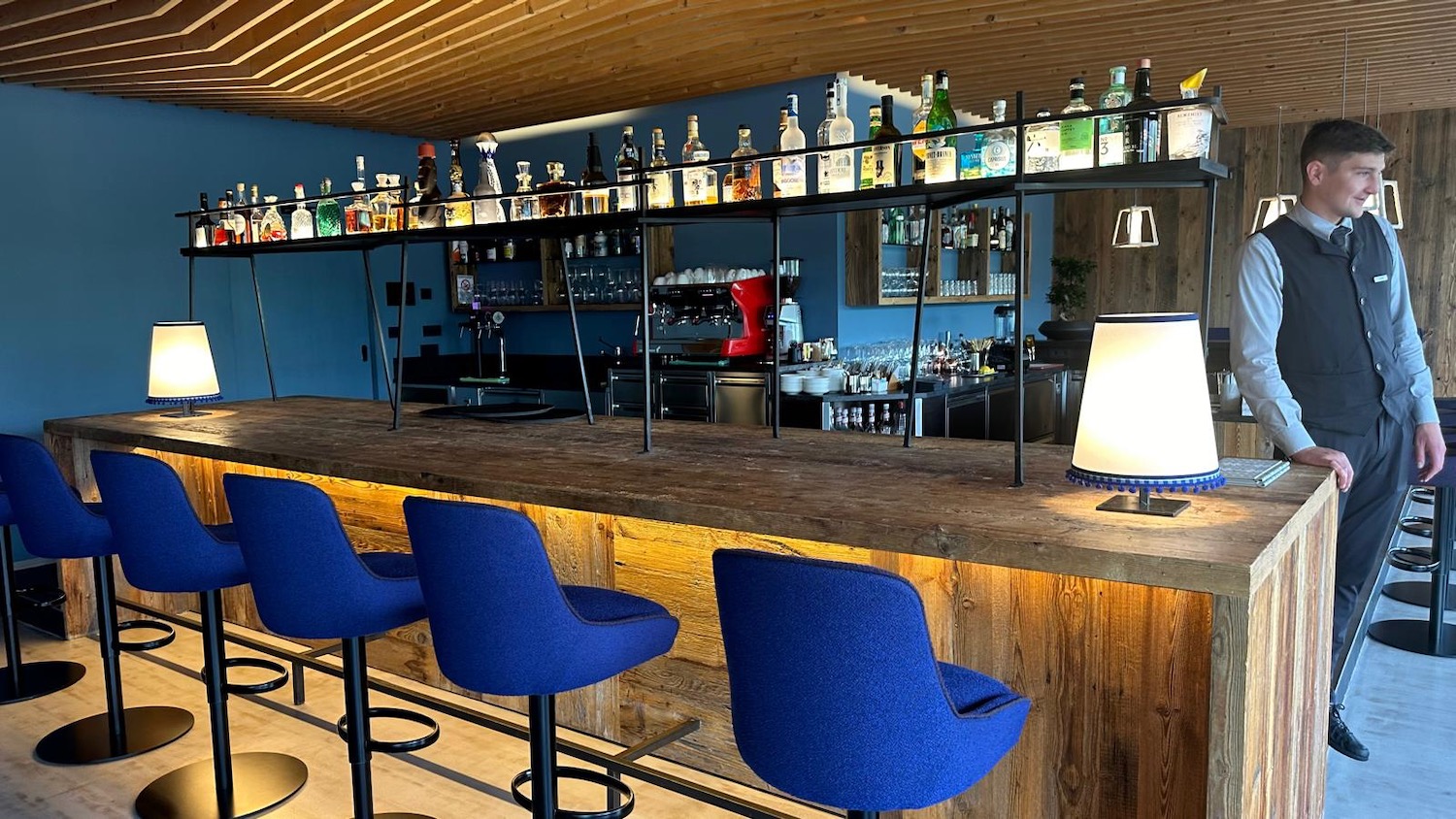 a bar with blue chairs and a shelf with bottles on it