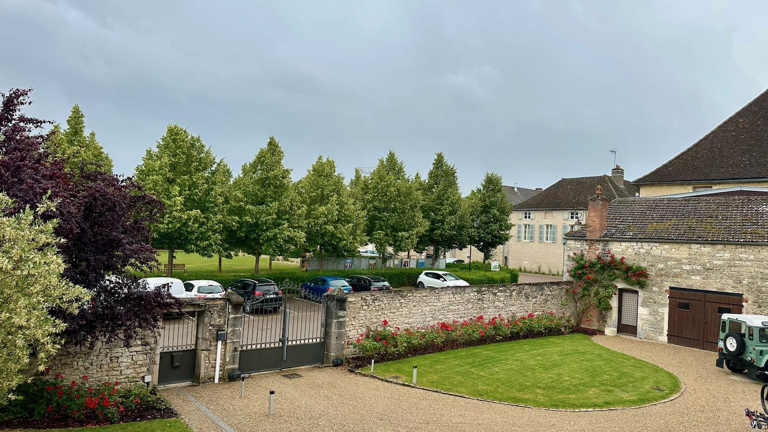 a driveway with a stone wall and a lawn with cars parked in the back