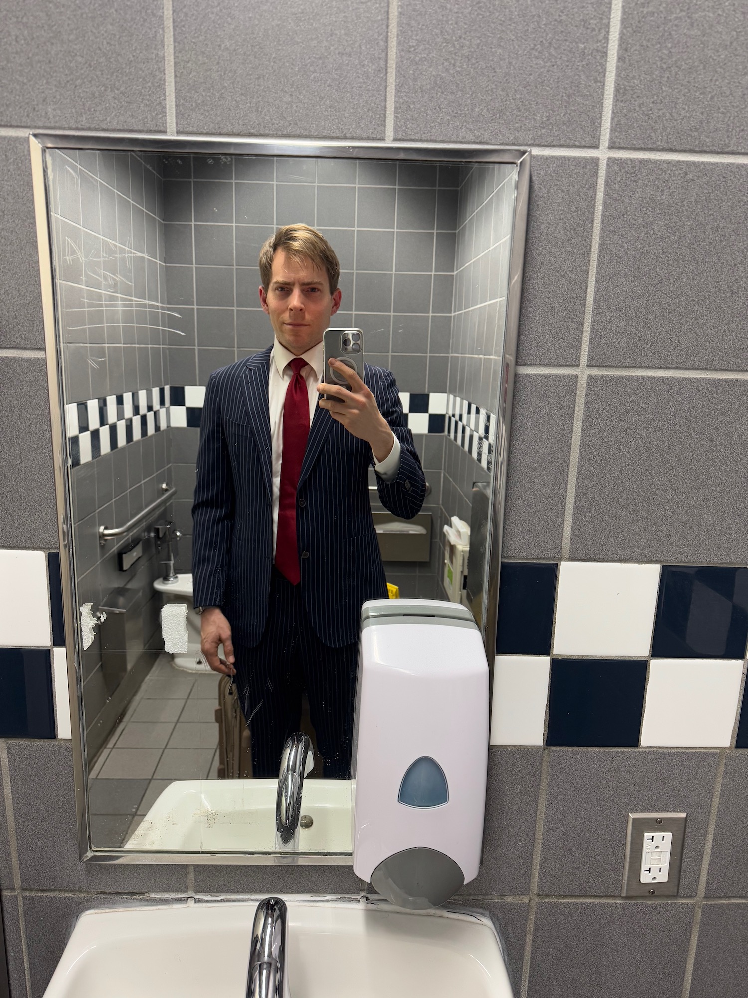 a man in a suit taking a selfie in a bathroom mirror