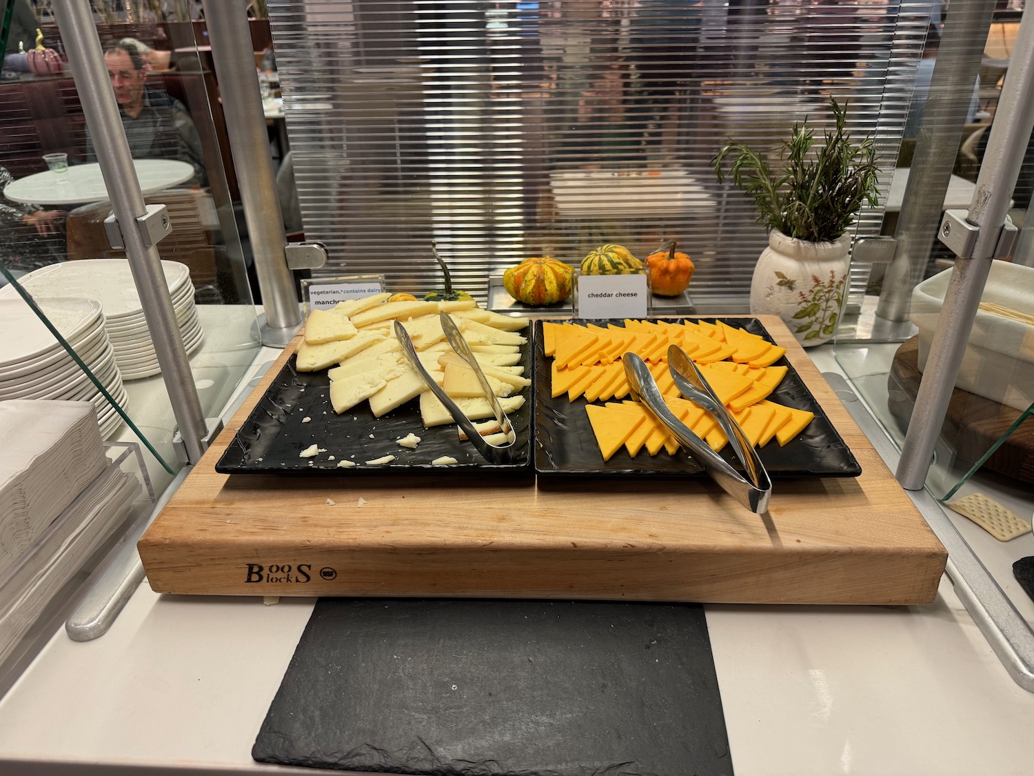 a tray of cheese and tongs on a wooden board