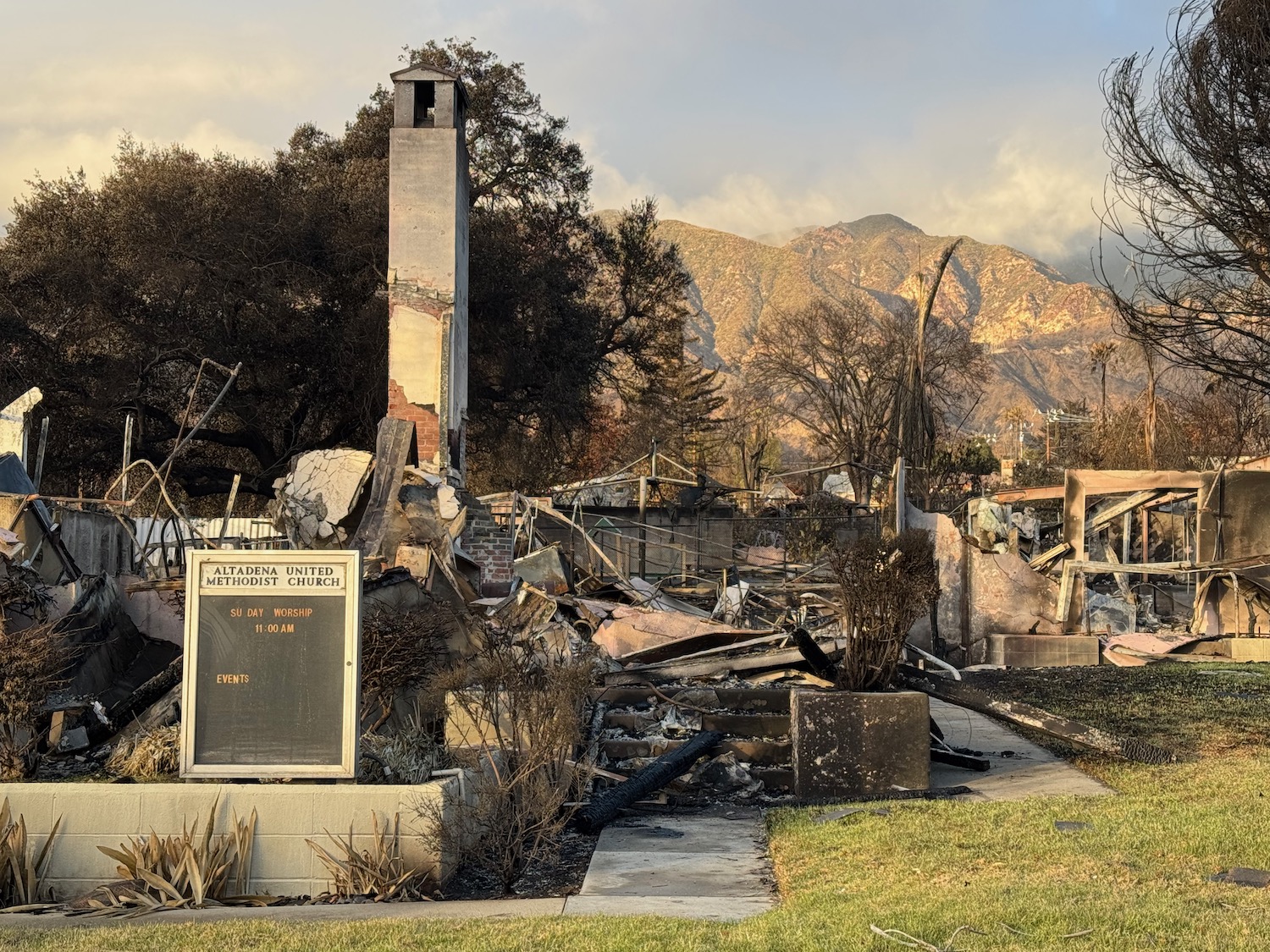 a burned down house with a sign and a mountain in the background