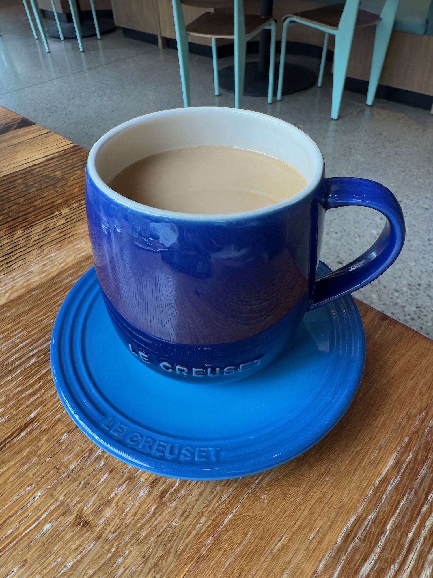 a blue mug with a brown liquid on a saucer on a wooden table