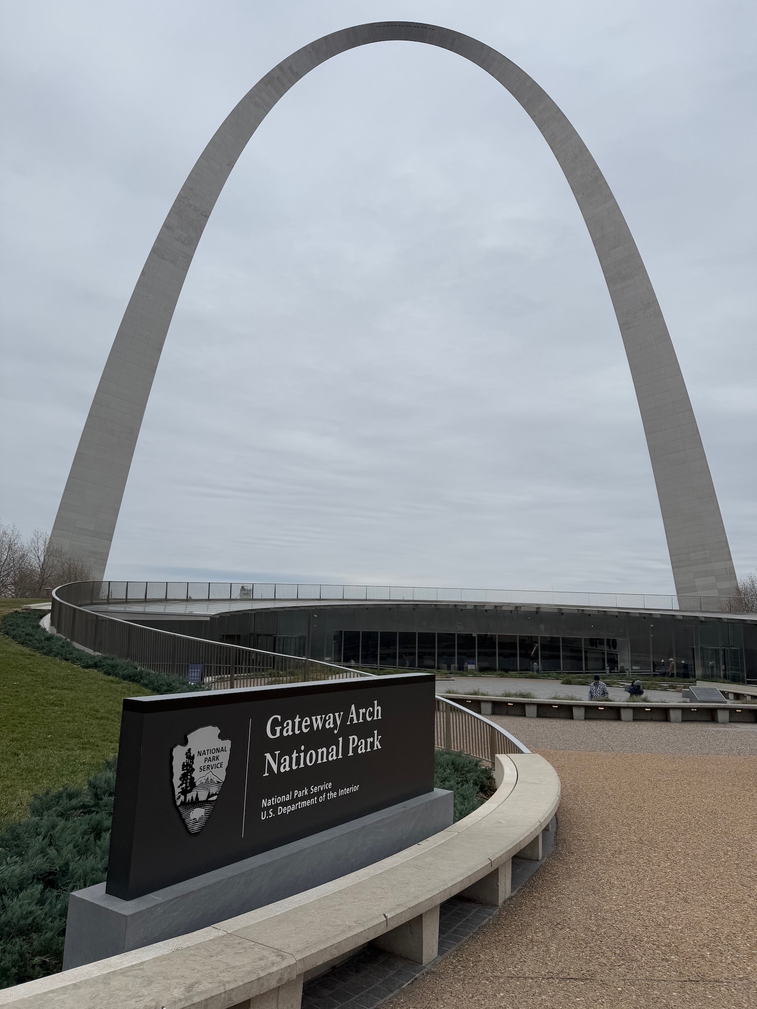 a large arch with a sign with Gateway Arch in the background