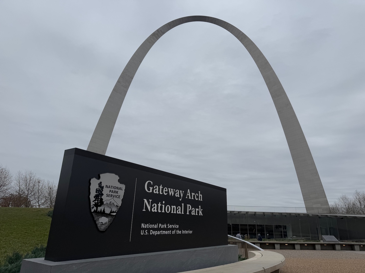 a sign with a large arch in the background with Gateway Arch in the background