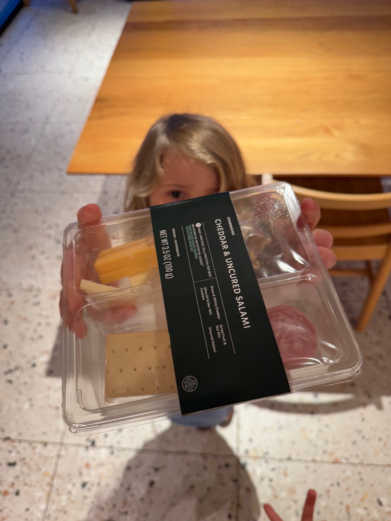 a child holding a plastic container with cheese and meat