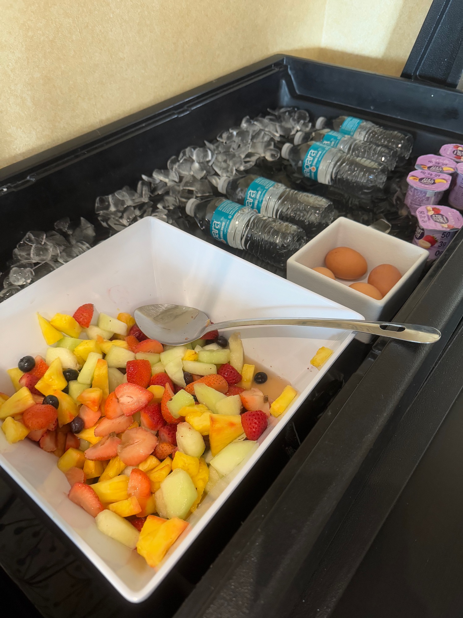 a bowl of fruit and eggs in ice with water bottles and yogurt