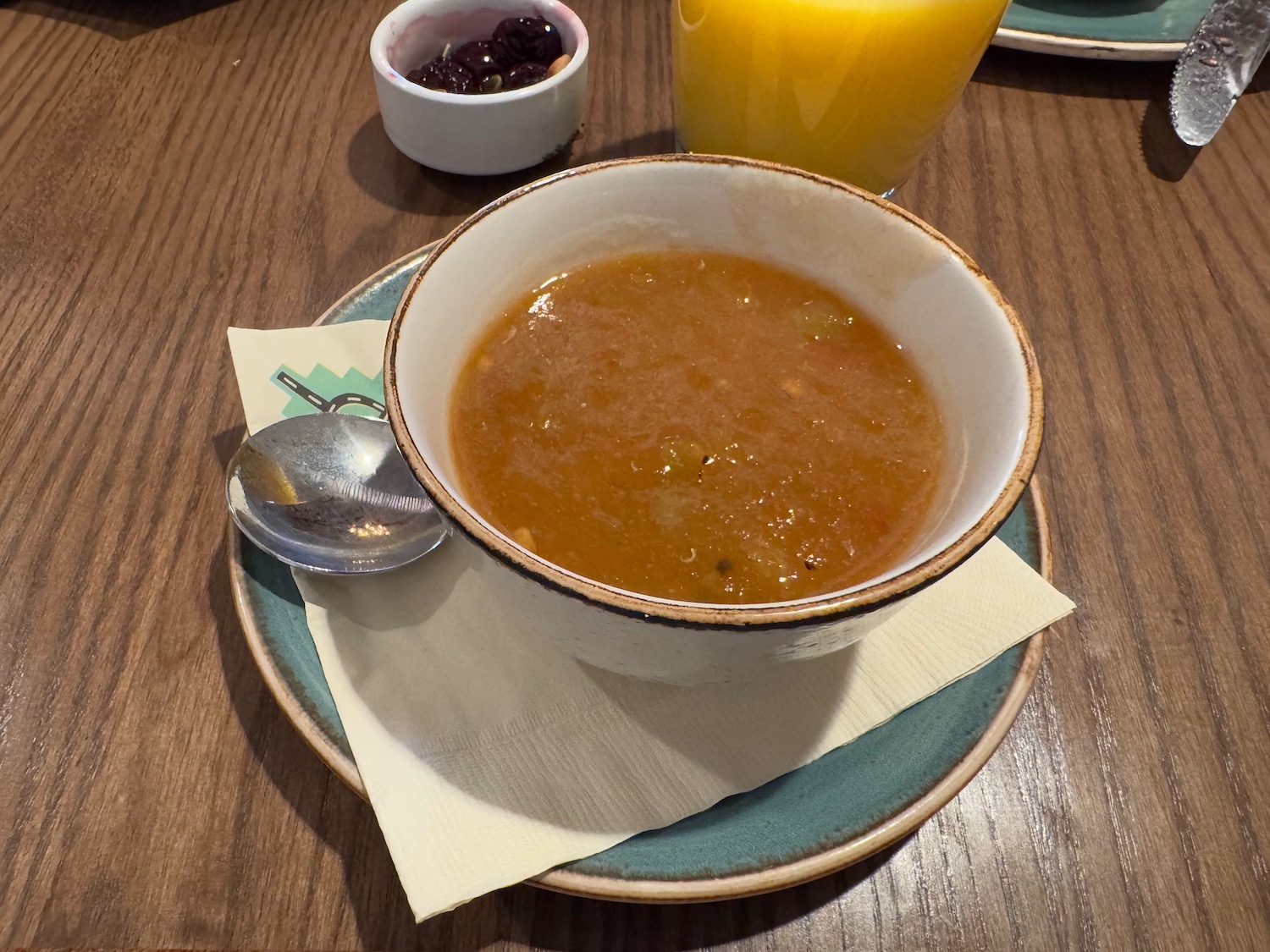 a bowl of soup on a plate with a glass of orange juice and a spoon