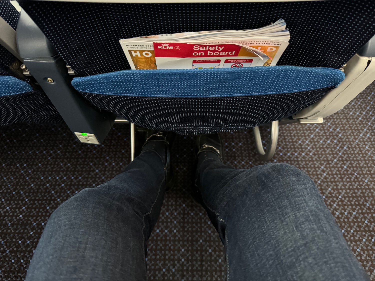 a person's legs and a seat with a magazine in the back