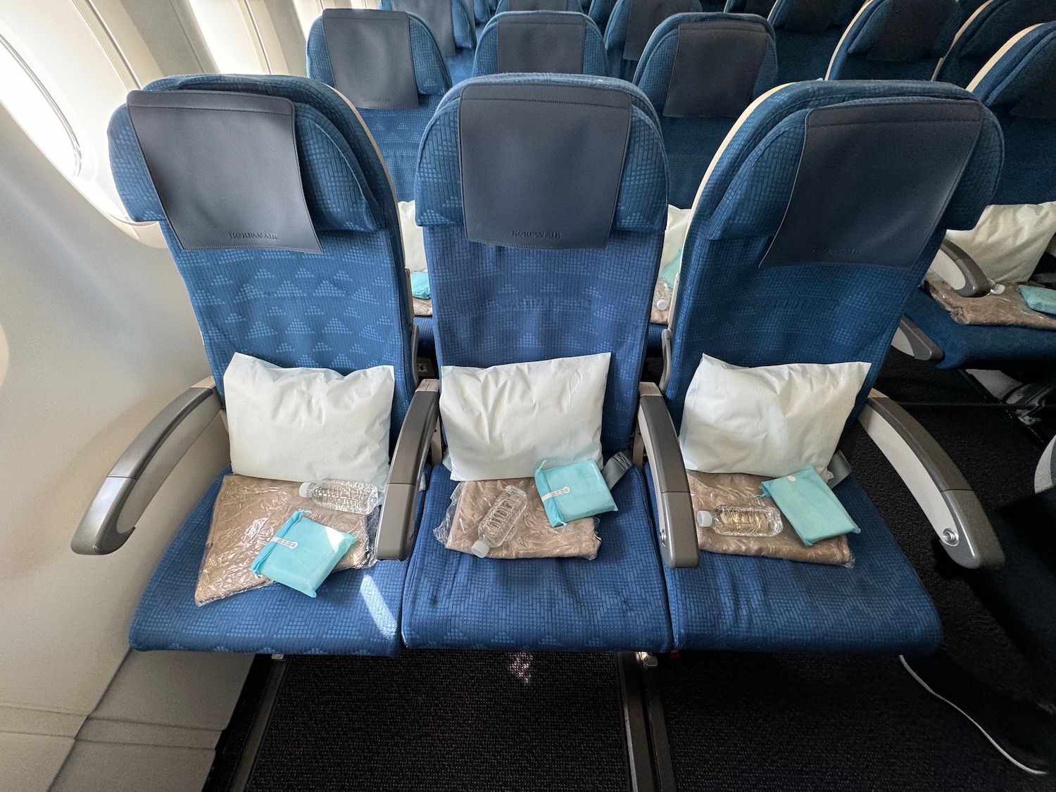 a row of blue seats with white pillows and a white bag on it