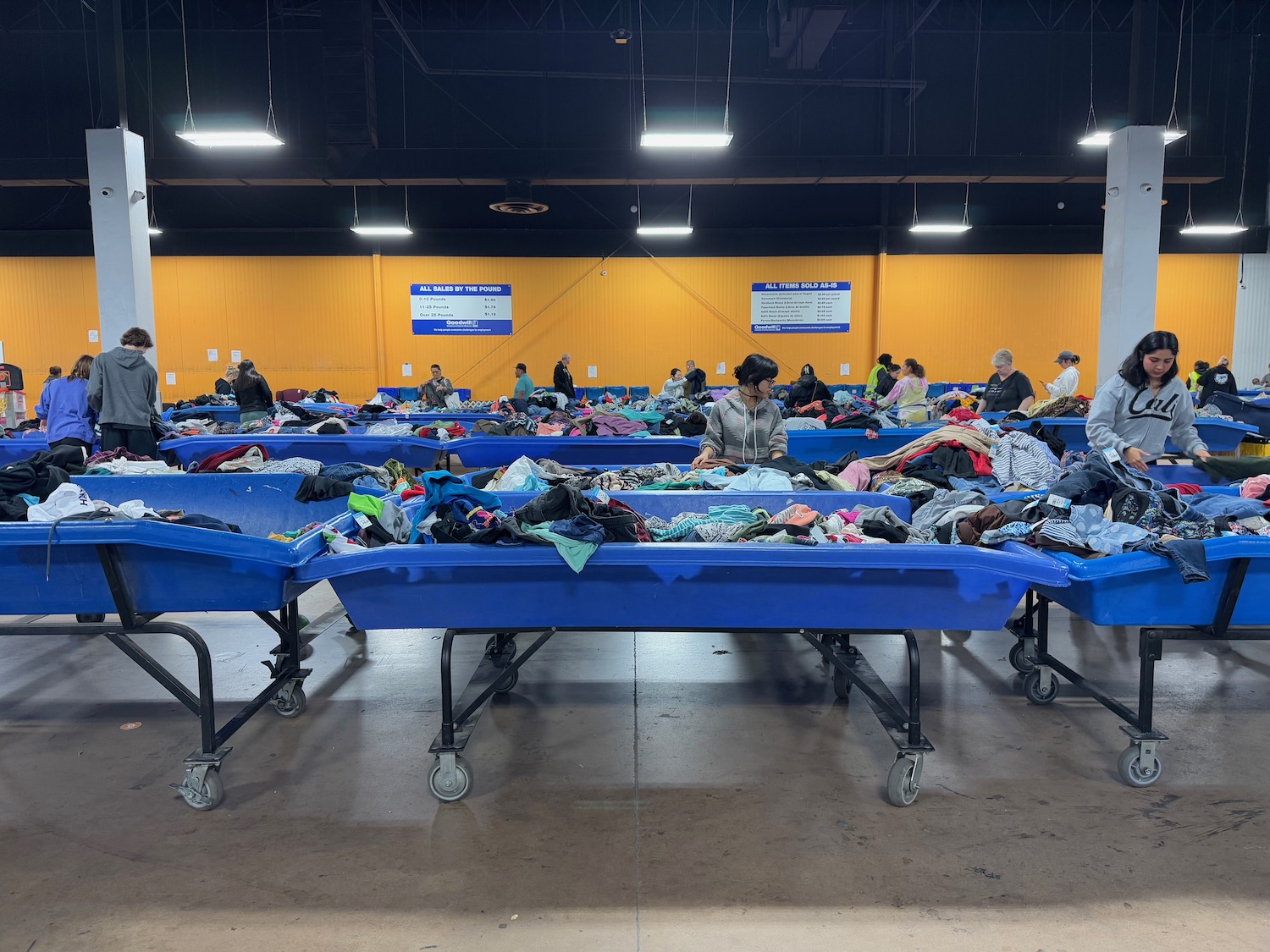 a group of people sitting in a room with blue carts with clothes