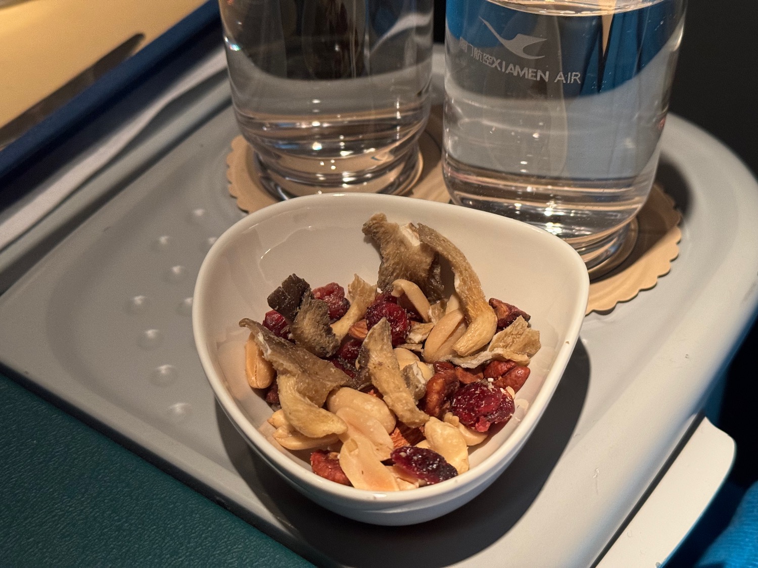 a bowl of nuts and dried fruit next to a glass of water