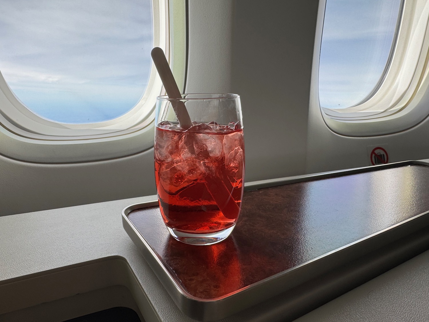 a glass with red liquid and ice on a tray on a plane