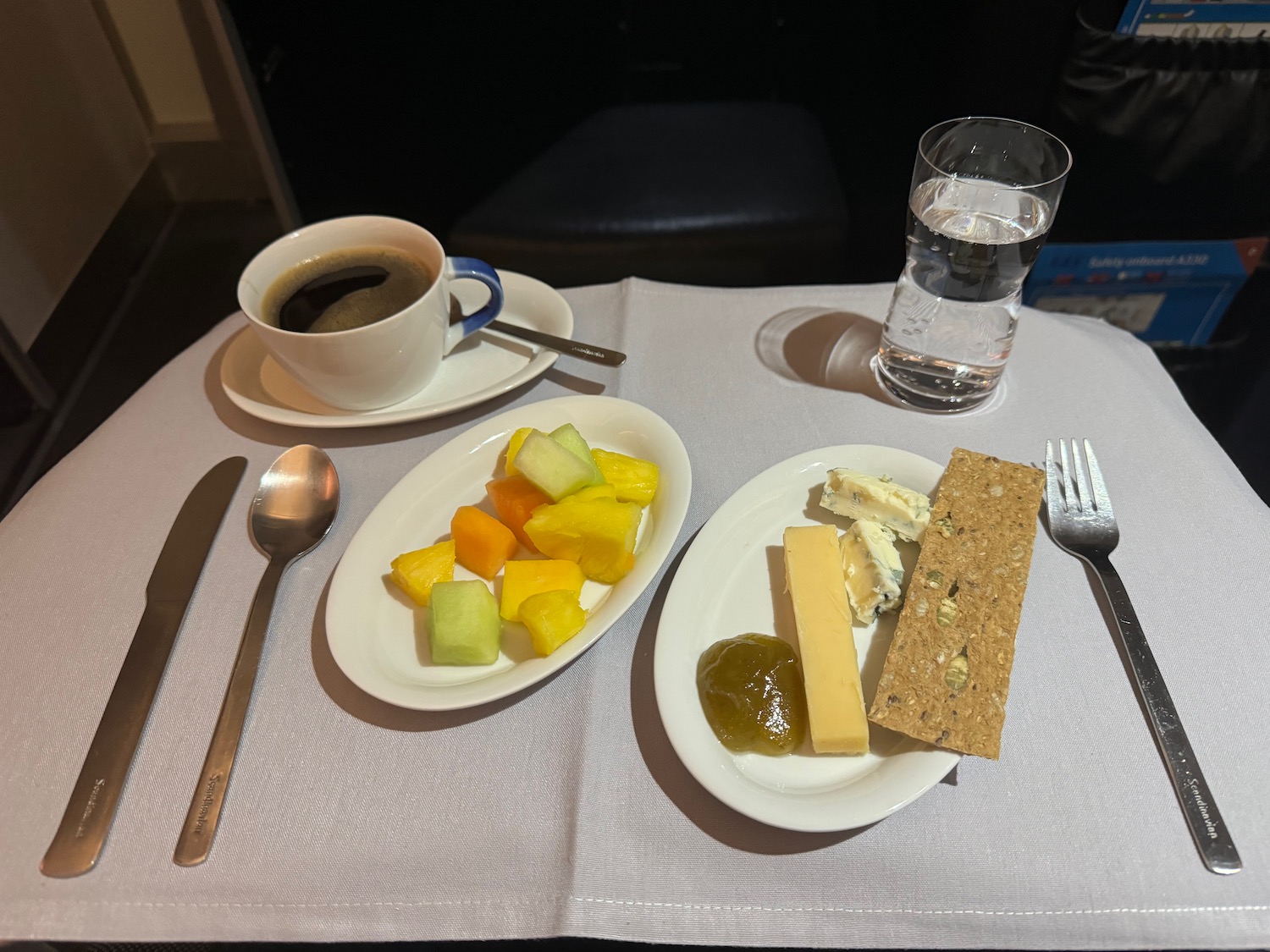 a plate of fruit and cheese on a table with a cup of coffee and a spoon