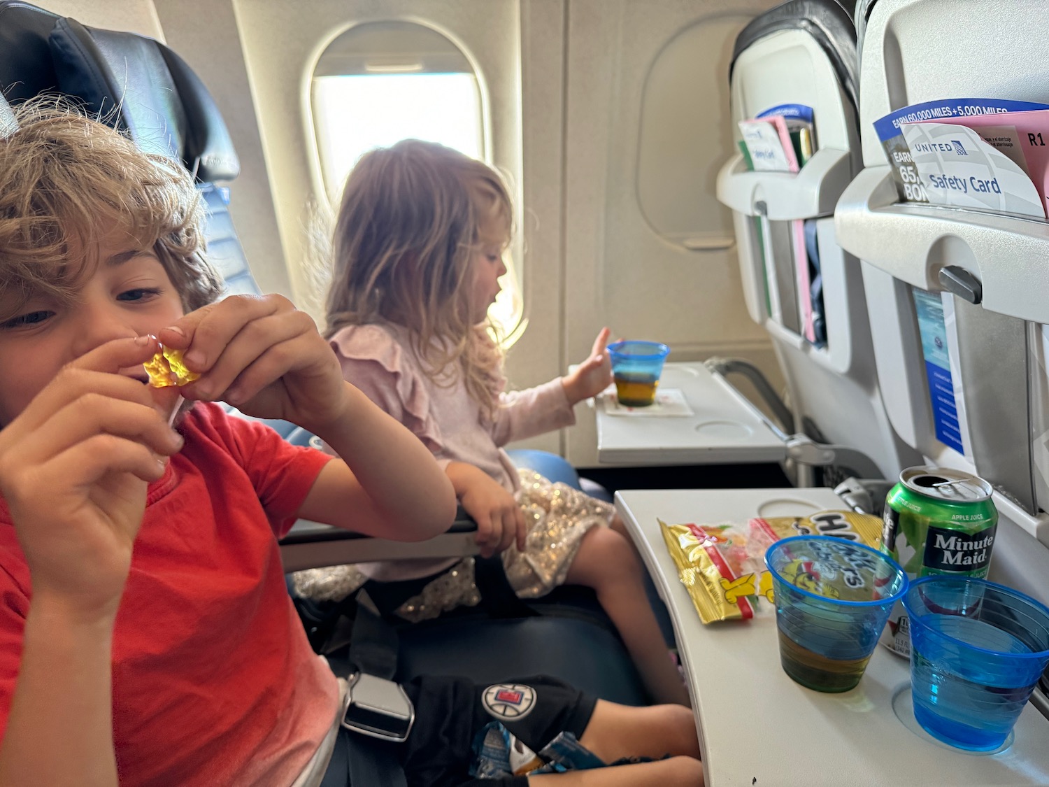 a boy and girl sitting in an airplane eating food