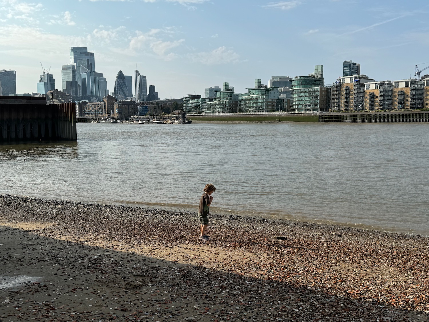 a child standing on a beach near water with a city in the background