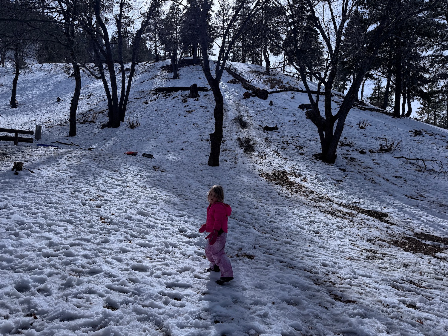 a girl in pink snowsuit walking in a snowy hill