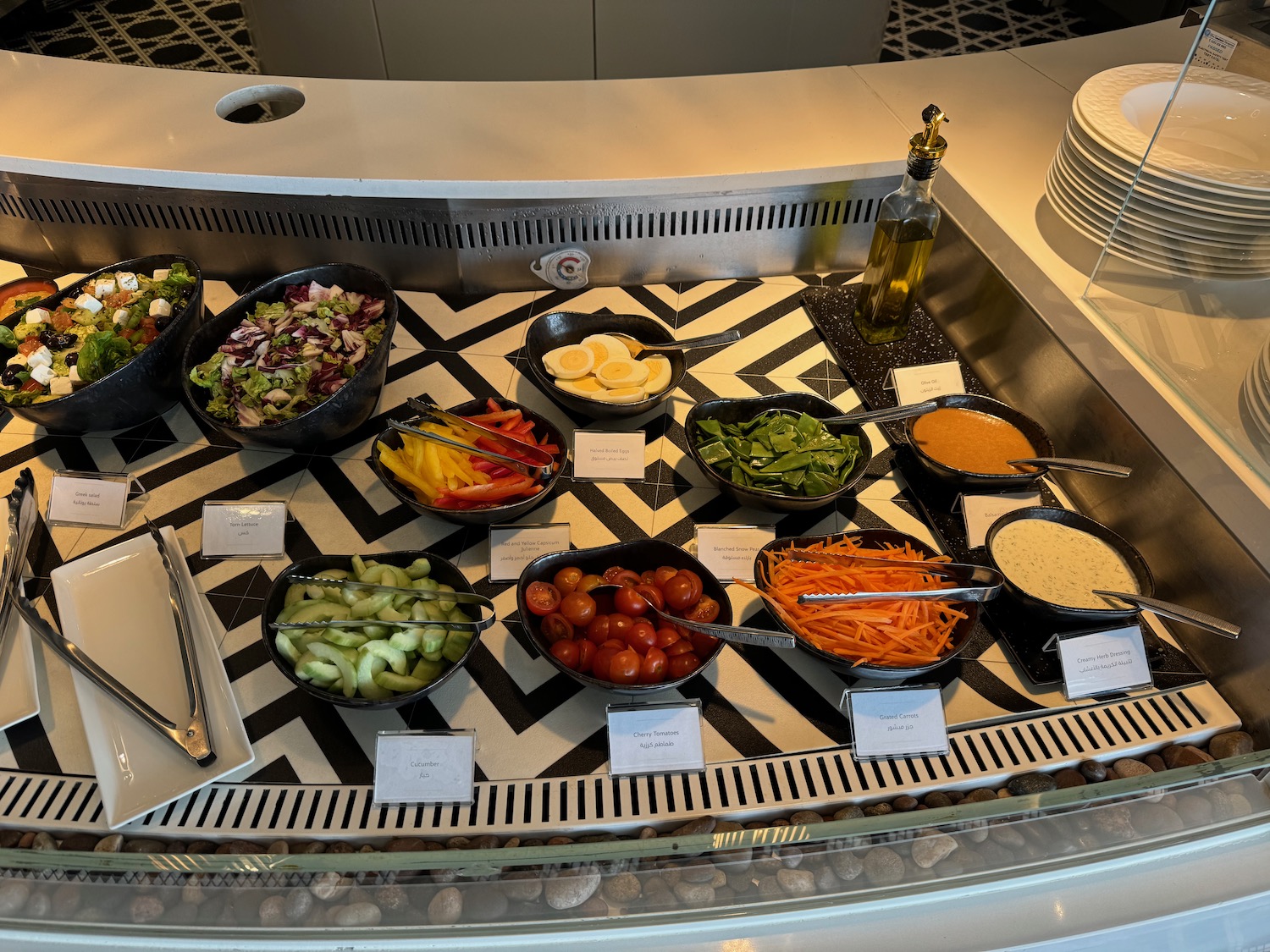 a salad bar with bowls of vegetables and a bottle of oil