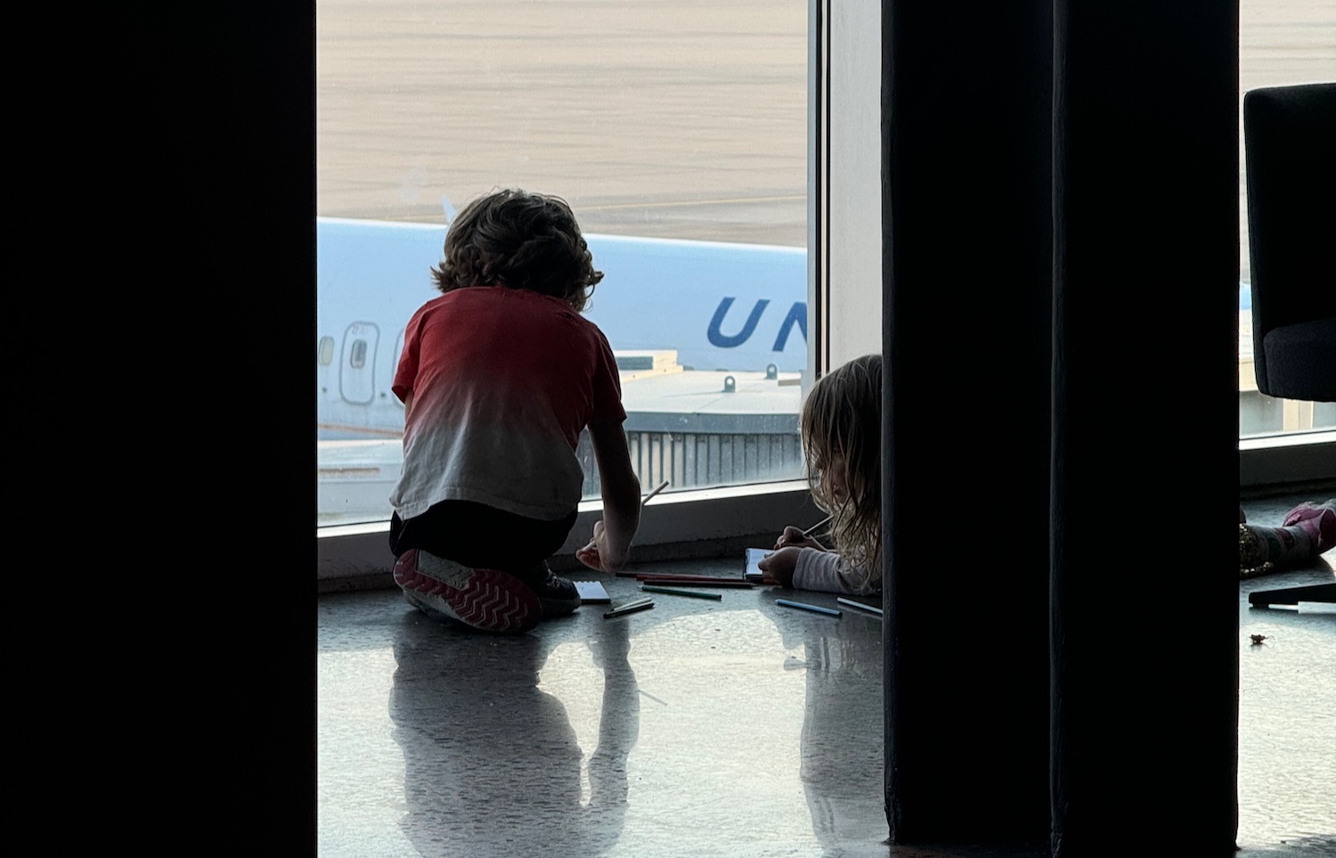 a two children sitting on a floor looking out a window