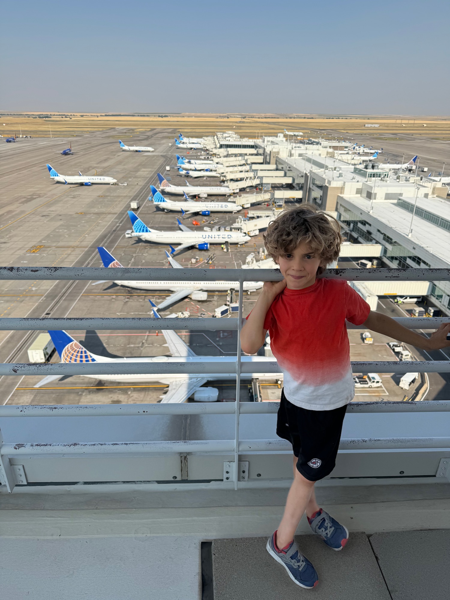 a boy standing on a railing with planes in the background