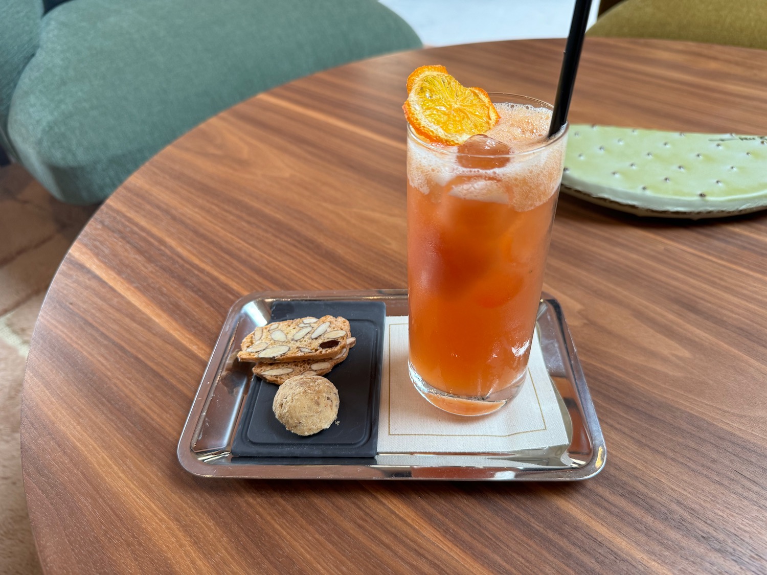 a glass of orange drink with a straw and a cookie on a tray